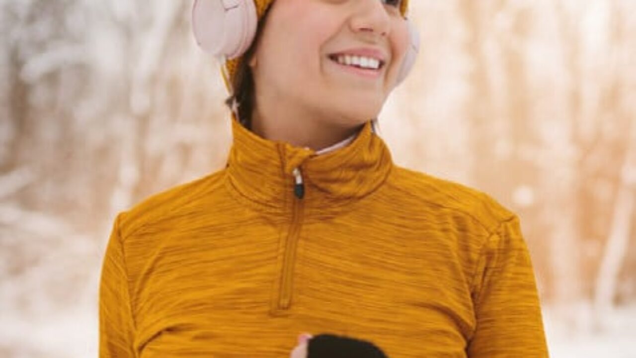 junge Frau mit Wolljacke und Mütze beim Joggen im verschneiten Wald