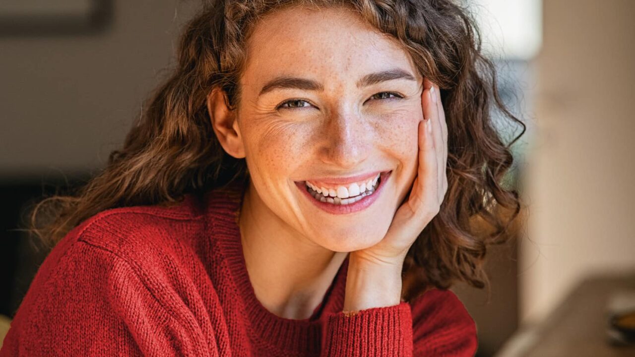 freudig lächelnde junge Frau mit rotem Wollpullover